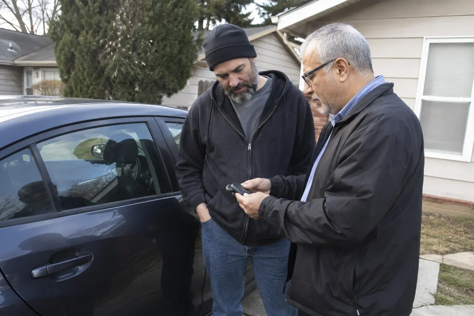 Two adults discussing a key fob beside a parked car. — Car Lockout Service, Toronto